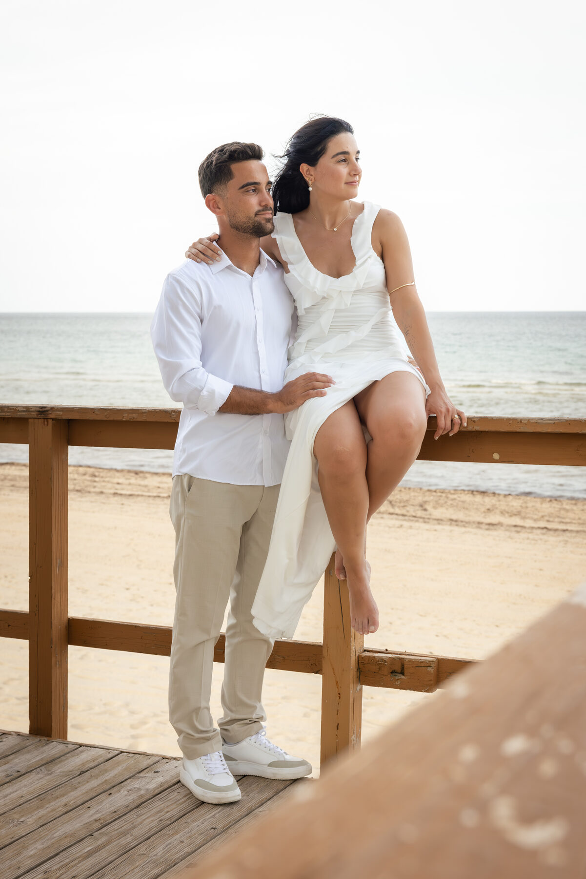 Pareja sentada sobre una baranda de madera frente a la playa